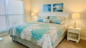 A bedroom with a bed, two bedside tables, a window with blinds, and two wall-mounted pictures.