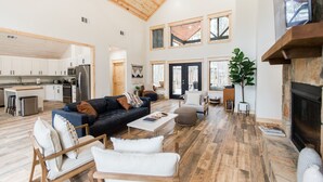 Un salón amplio con techo de madera, chimenea y cocina al fondo.