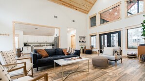 Amplia sala de estar con techo alto, vigas de madera y ventanas grandes.
