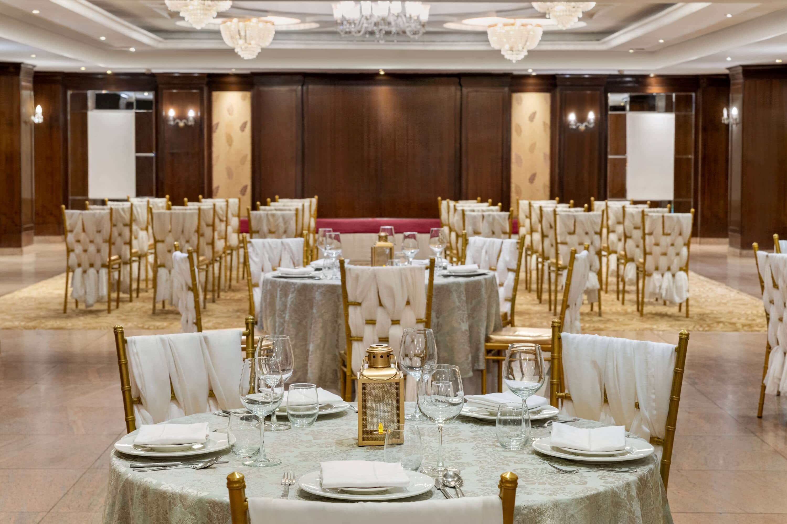 Un salón de banquetes con mesas redondas, sillas doradas y candelabros.