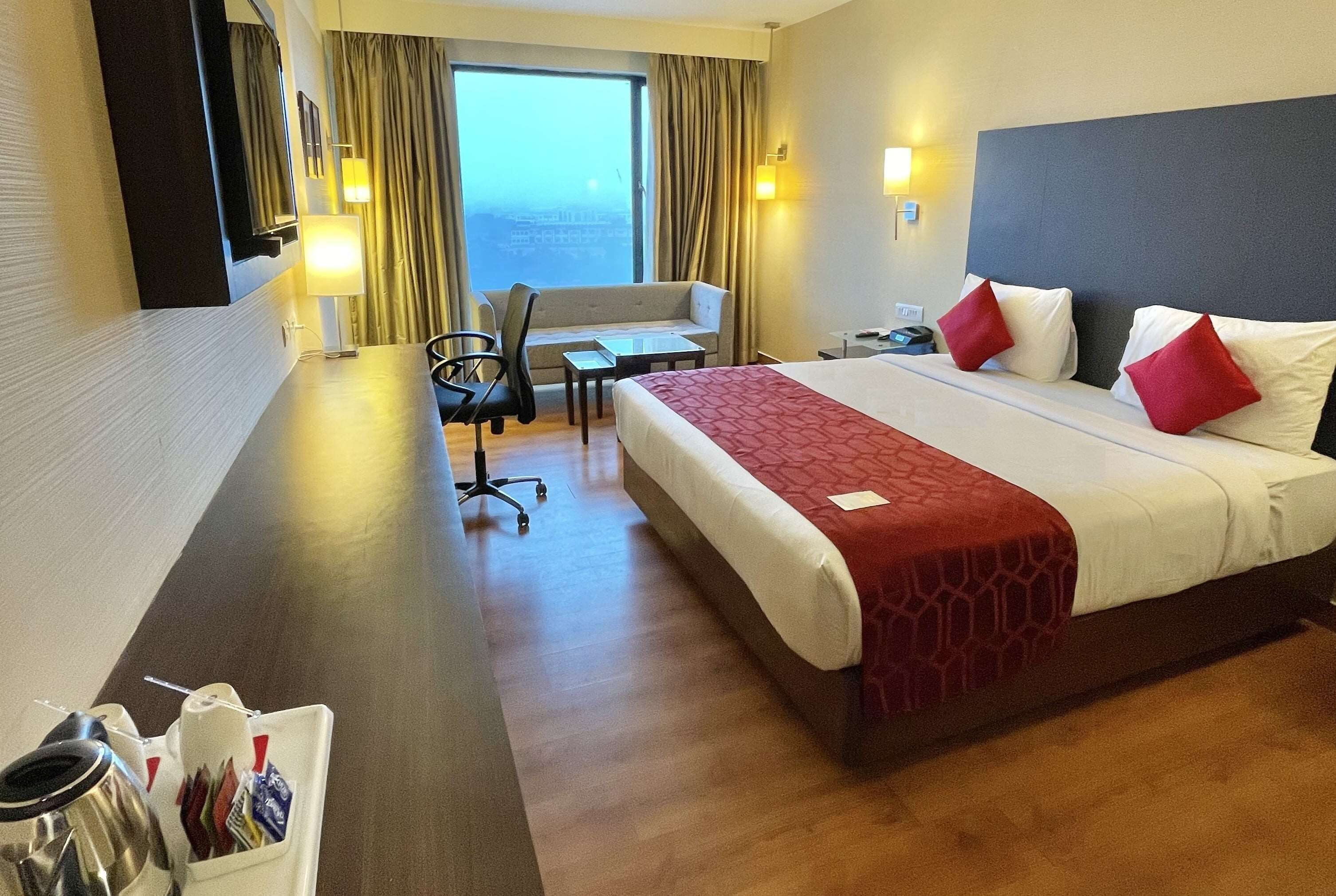 Habitación de hotel con una cama grande, un escritorio, una silla y vistas a la ciudad.