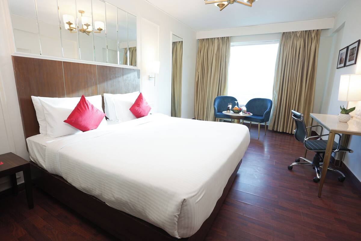 A hotel room with a large bed, a desk, a chair, and a view of the outdoors.