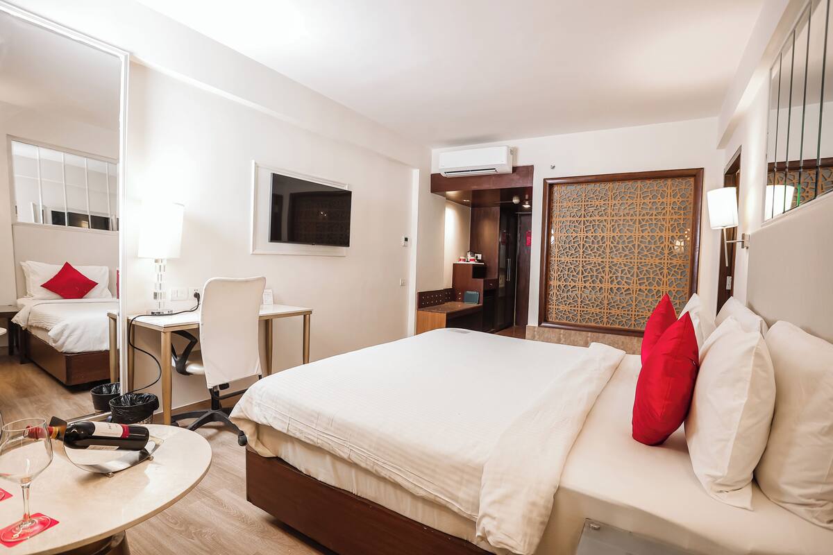 A hotel room with a bed, a desk, a chair, a TV, and a minibar.