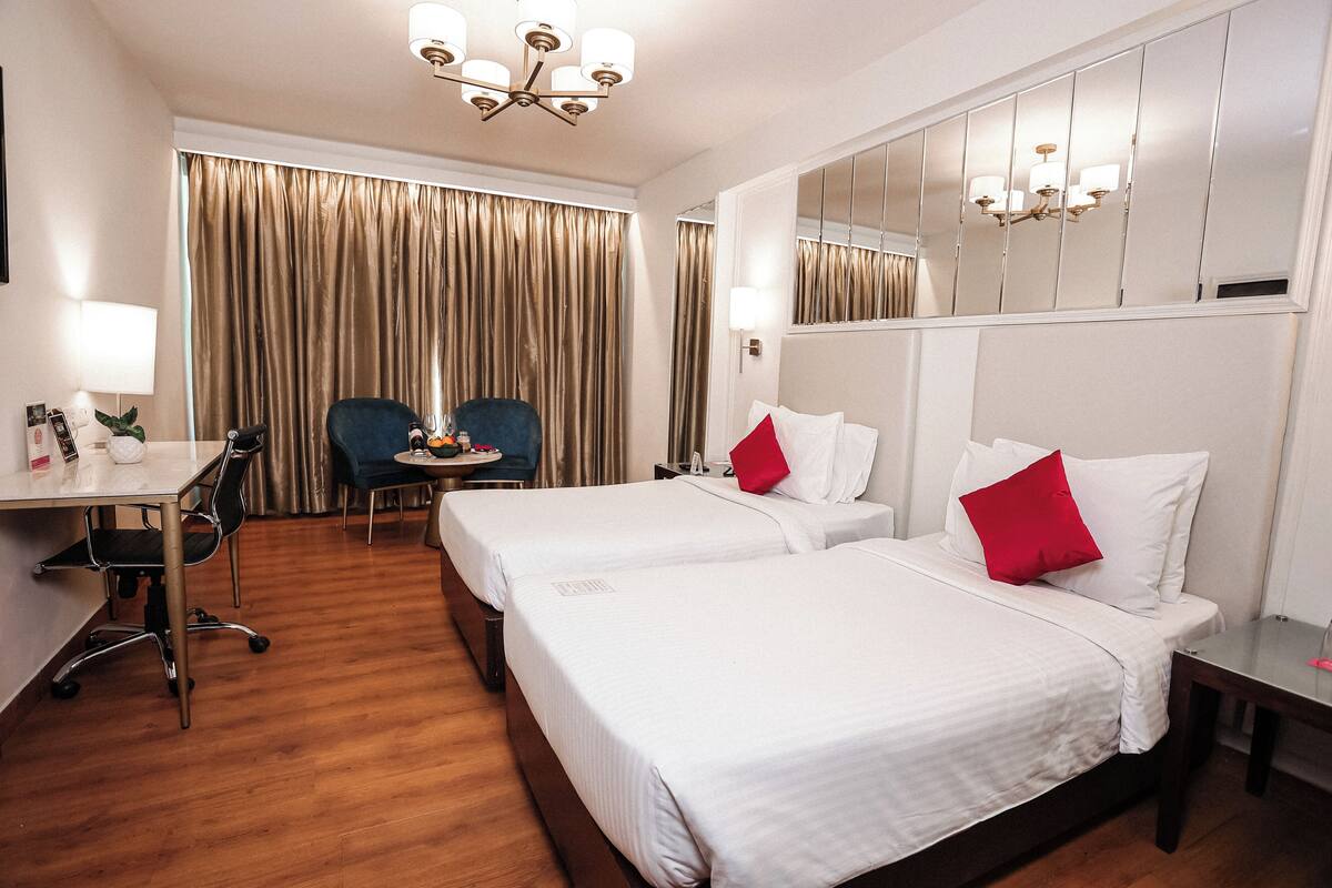 A hotel room with two beds, a desk, a chair, a small table, and a large mirror.