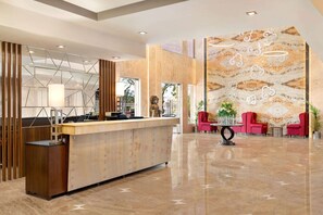 A modern hotel lobby with a reception desk, red seating, and a decorative wall with geometric patterns. - Ramada by Wyndham Jaipur North (Jaipur)