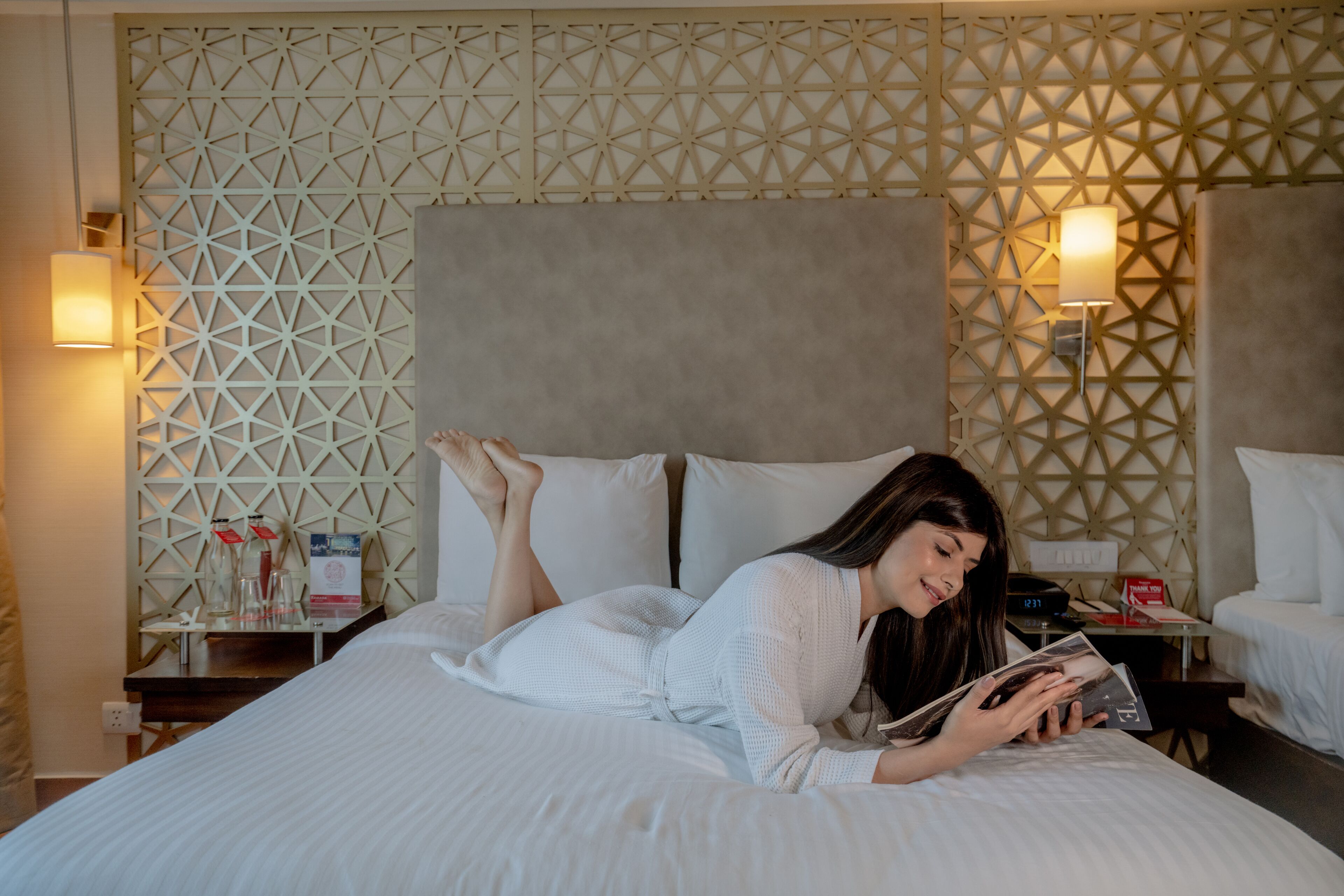 Une chambre d’hôtel avec un mur orné d’un motif géométrique, un lit avec une literie blanche et deux tables de chevet avec des lampes.
