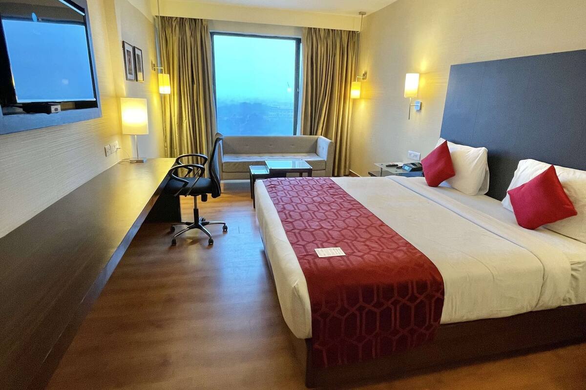A hotel room with a bed, a desk, a chair, a TV, and a window with curtains.