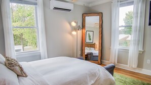 Et soveværelse med en stor seng, ventilator, klimaanlæg, et spejl og et vindue med gardiner.