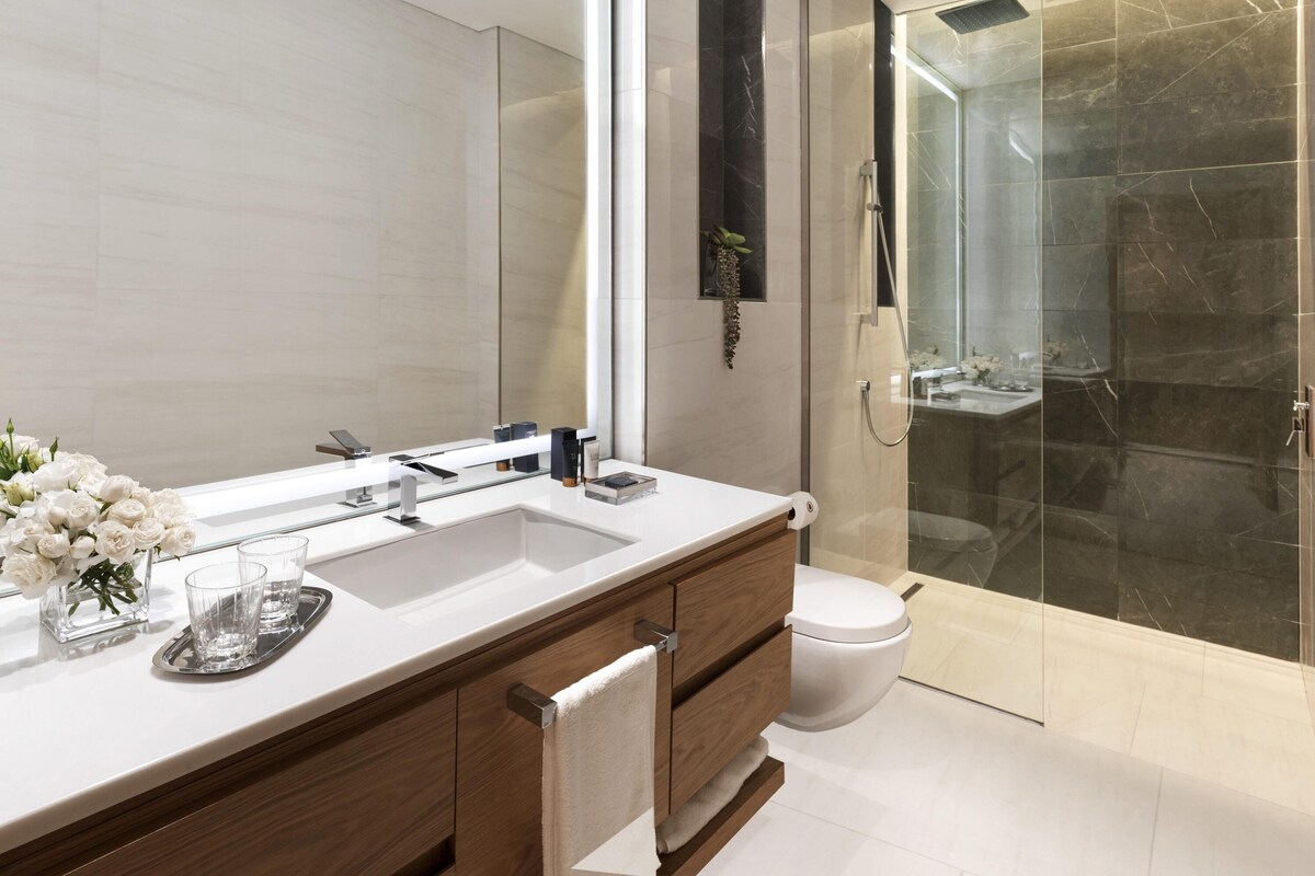 A modern bathroom with a large mirror, a white sink, a glass shower enclosure, and a toilet.