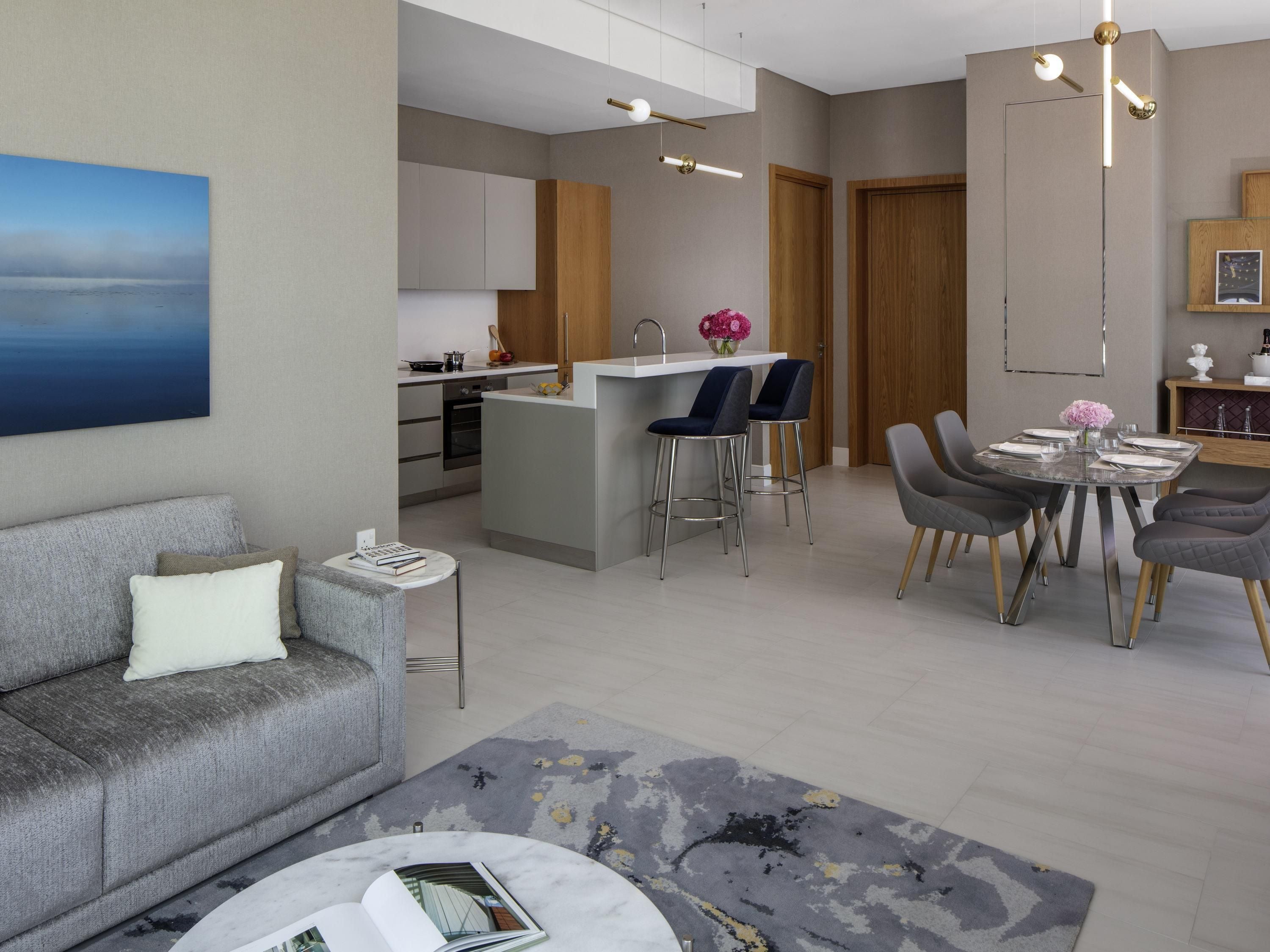 A modern living room with a grey sofa, a coffee table with a book, and a dining area with a glass table and grey chairs.