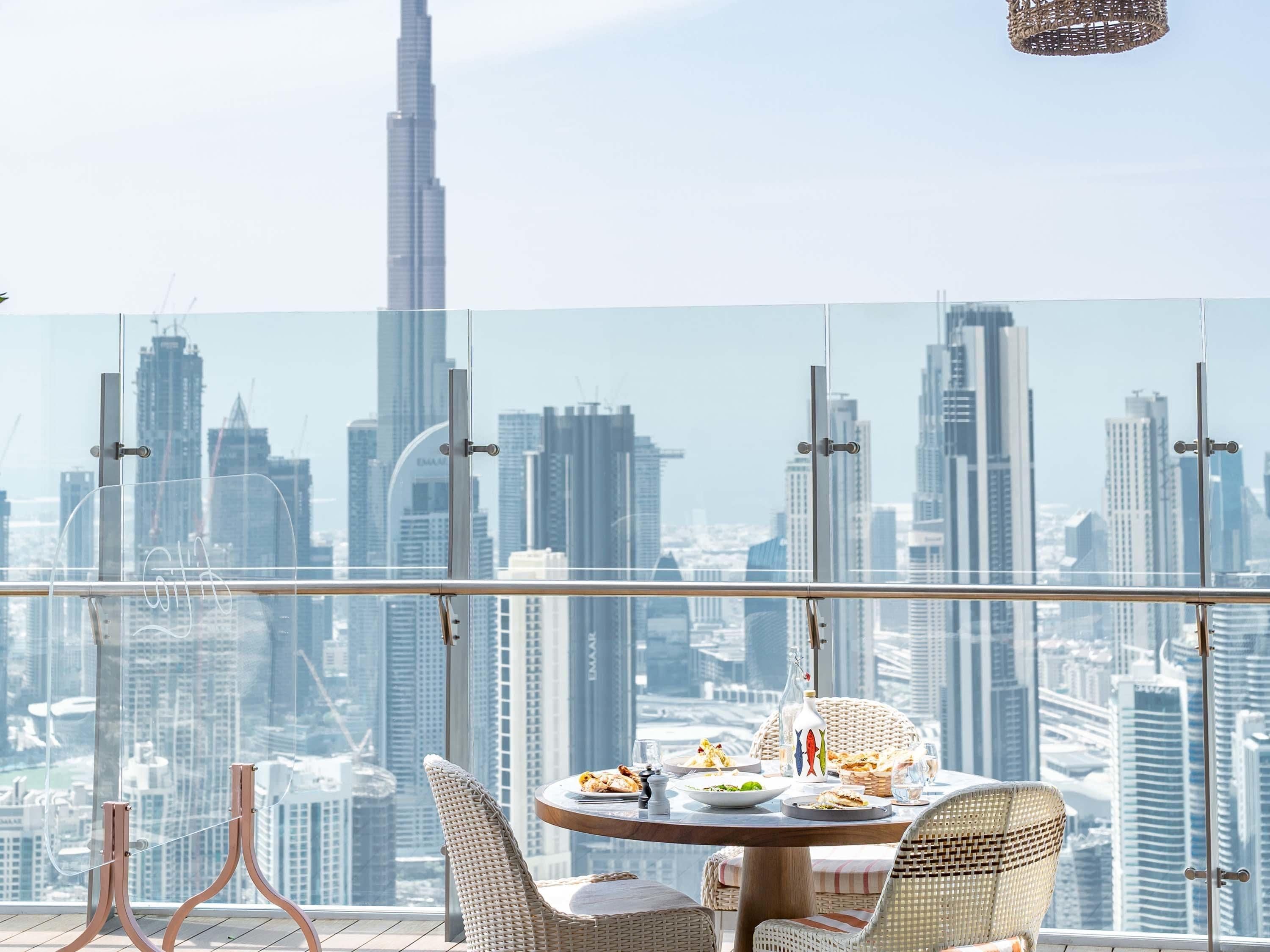 A dining area with a city view, featuring a round table with chairs and a glass railing.