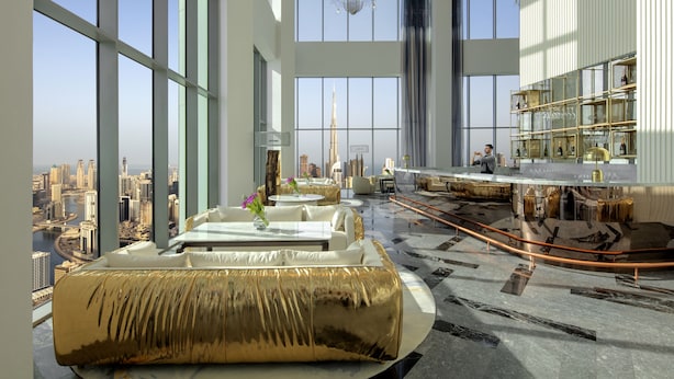 A spacious hotel lobby with large windows offering a city view, a central seating area with a golden sofa, and a bar with a glass railing. - SLS Dubai Hotel & Residences (Dubai)
