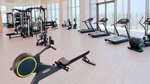 A gym with cardio machines, weight machines, and a large window with a view of a tall building. - SLS Dubai Hotel & Residences (Dubai)