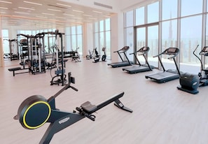 A gym with cardio machines, weight machines, and a large window with a view of a tall building. - SLS Dubai Hotel & Residences (Dubai)