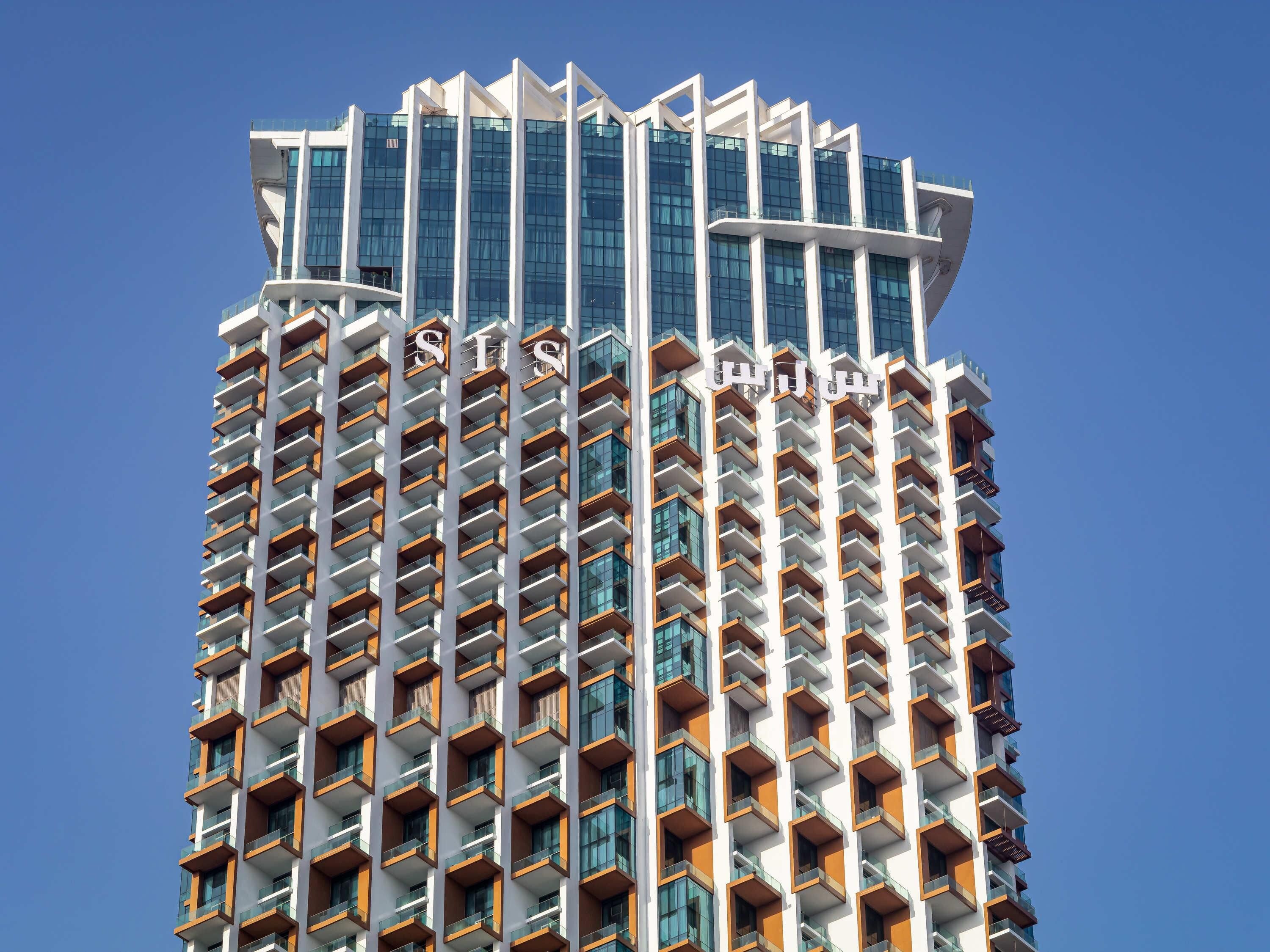 Un immeuble de grande hauteur doté d’une architecture moderne, avec de nombreux balcons et un ciel dégagé en arrière-plan.