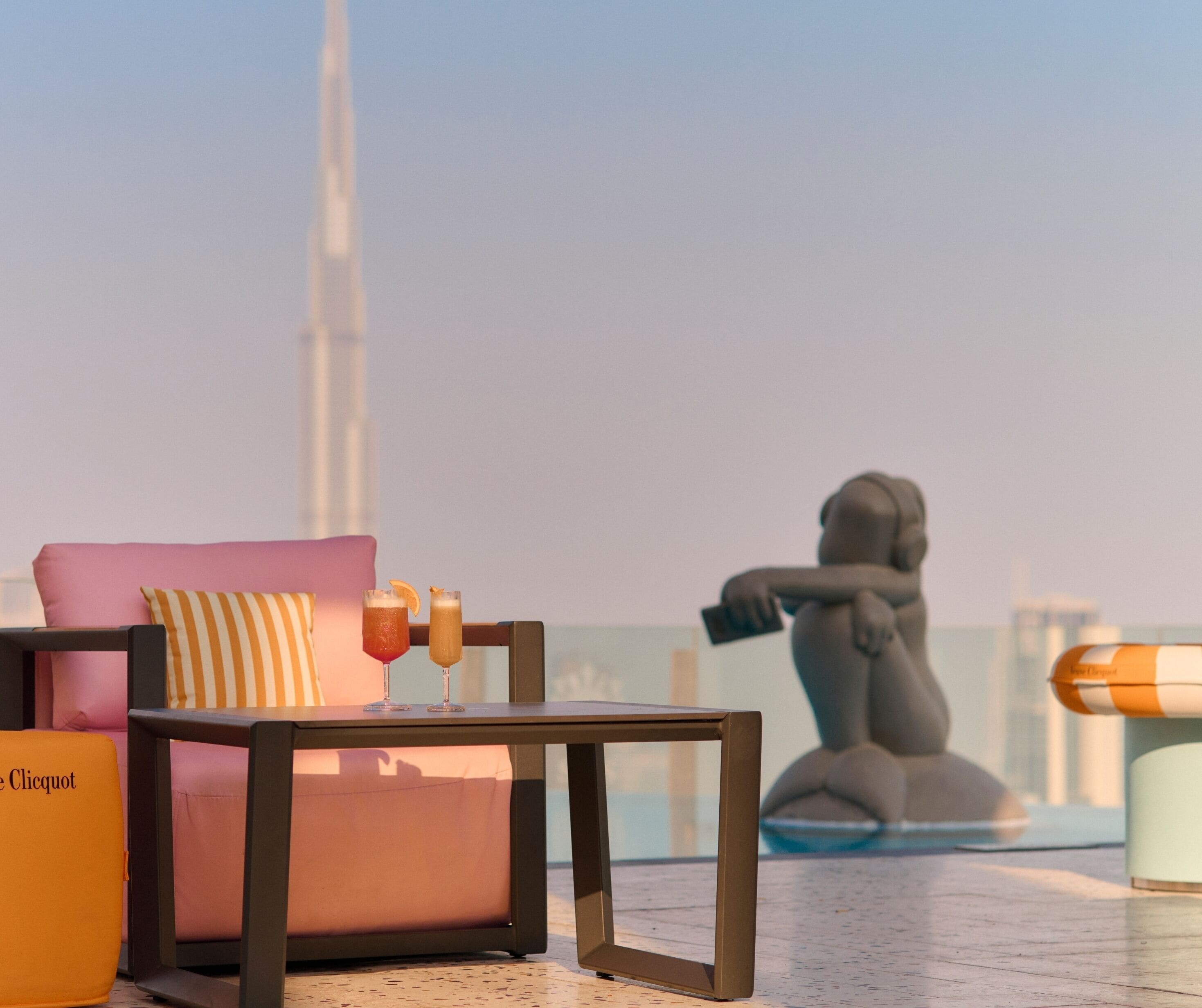 A modern outdoor seating area with a pink sofa, a small table with drinks, and a statue of a woman.