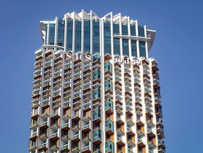 Un edificio alto de diseño arquitectónico moderno, con múltiples balcones y un cielo despejado al fondo.