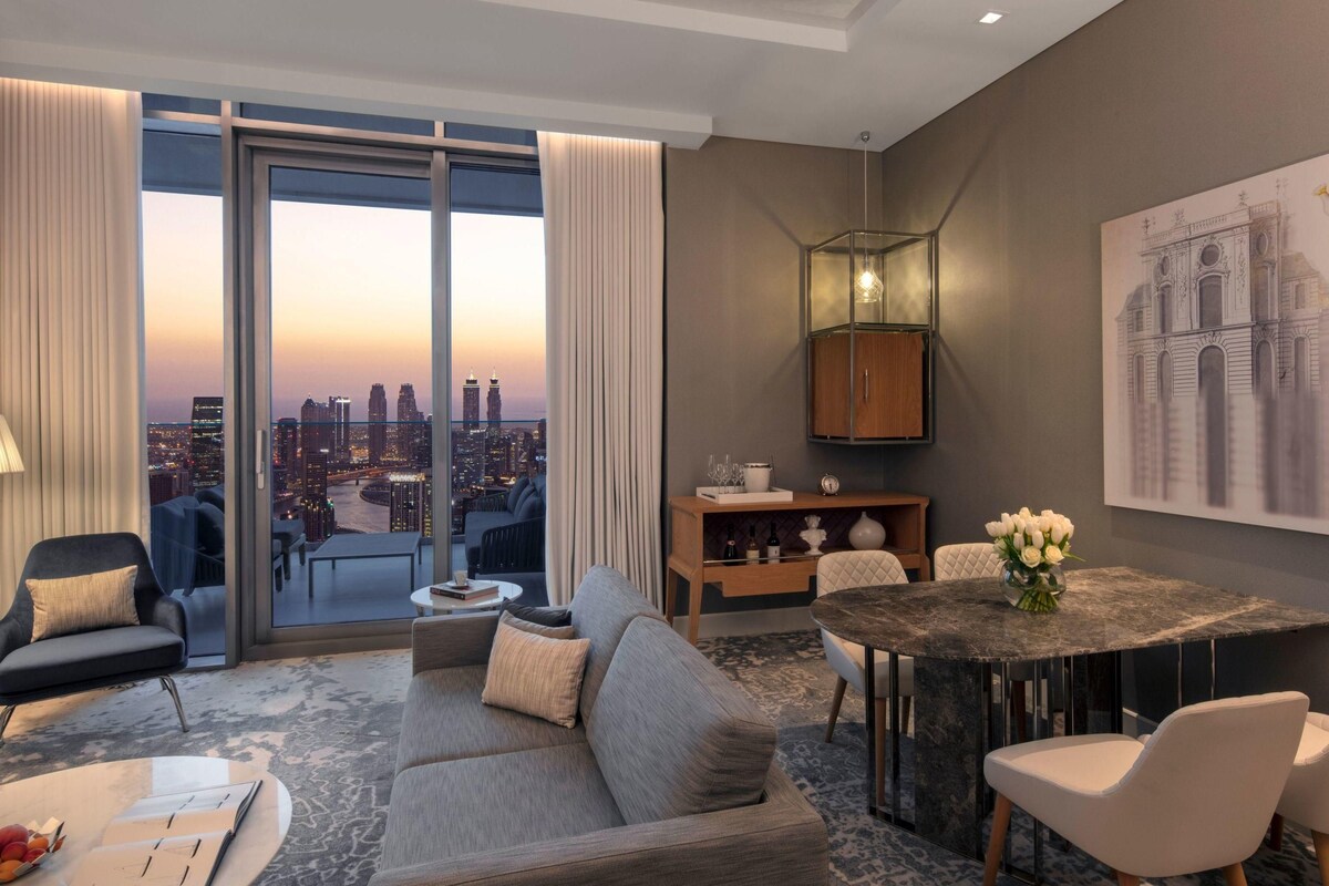 A modern hotel room with a city view, a dining area, and a large window with curtains.