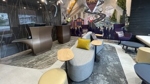 A modern hotel lobby with a reception desk, seating area, and a mural with a cityscape and a road leading to a hotel sign. - Mercure Auckland Queen Street (Auckland)