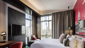 A modern hotel room with a large bed, a desk, a chair, a TV, and a cityscape view. - Mercure Auckland Queen Street (Auckland)