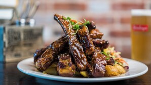 A plate of glazed ribs with sesame seeds and a side of potatoes, served on a white plate. - Mercure Auckland Queen Street (Auckland)
