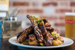 A plate of glazed ribs with sesame seeds and a side of potatoes, served on a white plate. - Mercure Auckland Queen Street (Auckland)