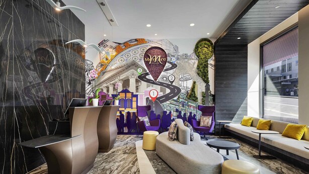 A modern hotel lobby with a reception desk, seating area, and a mural of a cityscape. - Mercure Auckland Queen Street (Auckland)