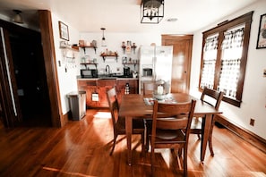 Eine Küche mit Holzboden, einem Esstisch mit Stühlen, einem Kühlschrank und verschiedenen Küchengeräten.