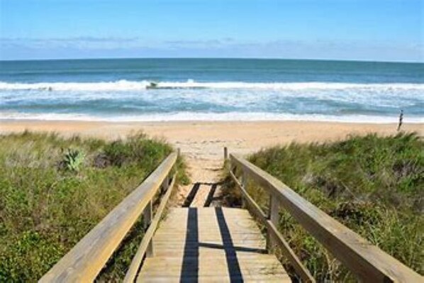A wooden boardwalk leading to a beach with waves in the background.
