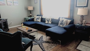 Una sala de estar con un sofá modular, una mesa de centro, una silla, una lámpara y una mesita auxiliar.