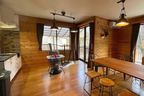 L’intérieur chaleureux d’un chalet avec une table à manger en bois, des tabourets de bar, une petite table ronde avec une bouilloire et une cheminée.