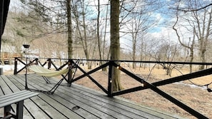 A wooden deck with a hammock and string lights, surrounded by trees.