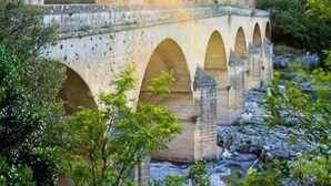 A stone aqueduct with multiple arches, surrounded by greenery.