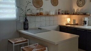 A modern kitchen with a central island, two bar stools, a hanging light, and decorative plates on the wall.