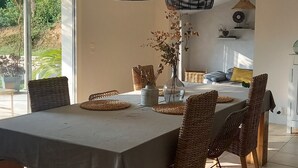 A dining area with a large table, wicker chairs, and hanging pendant lights.
