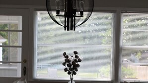 En matplats med ett bord och stolar, en hängande lampa och ett fönster med persienner.