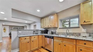 A modern kitchen with wooden cabinets, granite countertops, a dishwasher, and a window providing natural light.