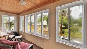 A sunroom with large windows, a ceiling fan, and a seating area with chairs and a bench.