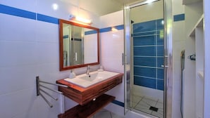 Een badkamer met een houten wastafelmeubel, een grote spiegel en een douche met glazen wanden.