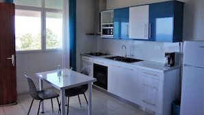 Een kleine keuken met witte en blauwe kastjes, een roestvrijstalen spoelbak en een eettafel met stoelen.