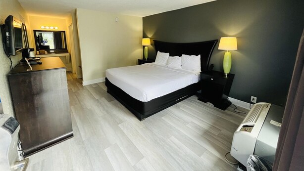 A hotel room with a bed, bedside lamps, a desk with a mirror, and a heater. - Rodeway Inn Silver Springs (Silver Springs)