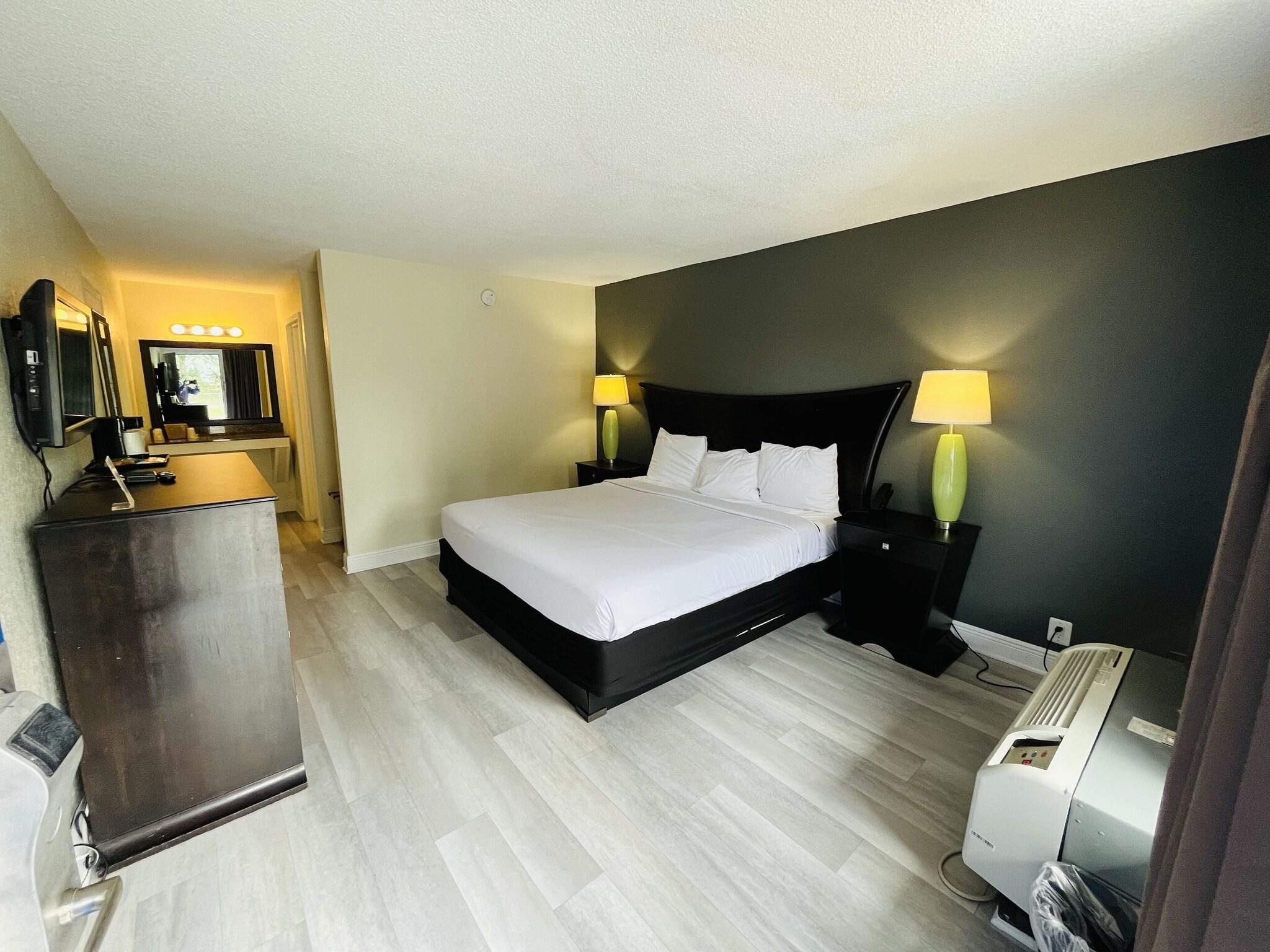 A hotel room with a bed, bedside lamps, a desk with a mirror, and a heater.