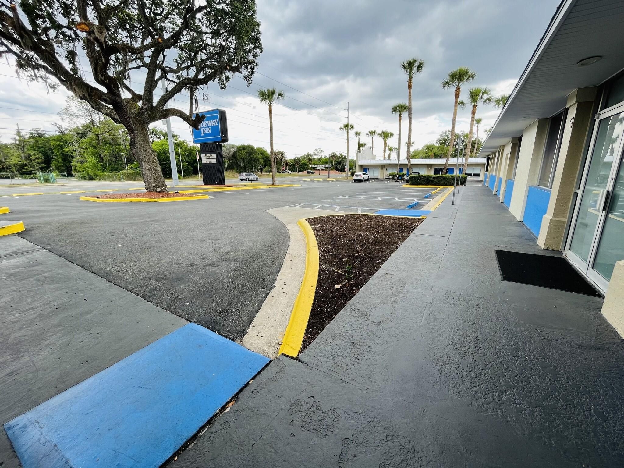 A parking lot with a blue and yellow curb, a sign for Wayfair Inn, and palm trees in the background.