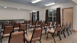 A conference room with rows of chairs, a projector screen, and a large window with curtains. - Rodeway Inn Silver Springs (Silver Springs)