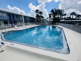 Una piscina con sillones de descanso y un edificio de fachada azul y blanca.