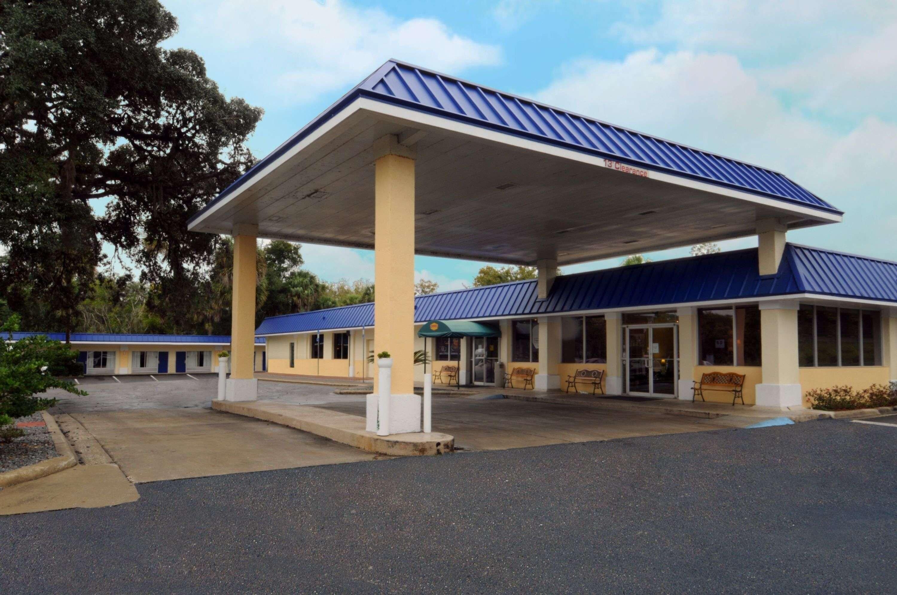 A motel with a covered parking area, a single-story building, and a blue roof.