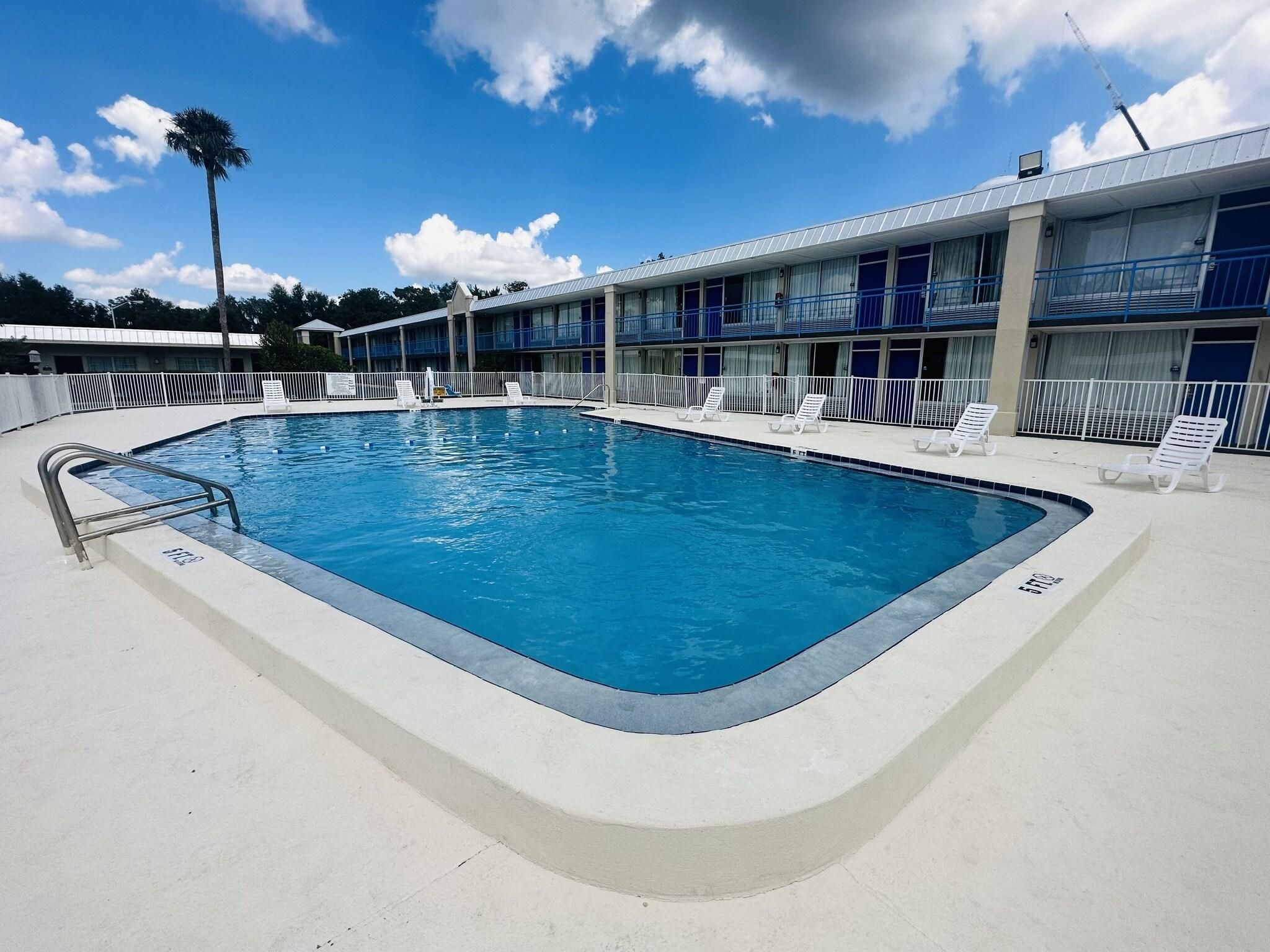 A swimming pool with a metal ladder, surrounded by a white fence. There are lounge chairs along the poolside.