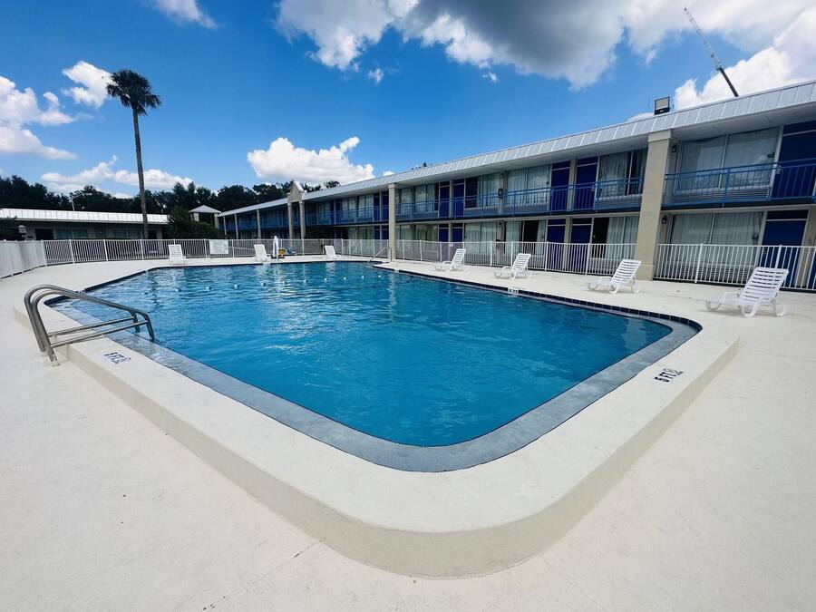 A swimming pool with a metal ladder, surrounded by a white fence. There are lounge chairs along the poolside.