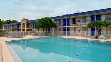 A hotel with a swimming pool, multiple balconies, and a clear sky.