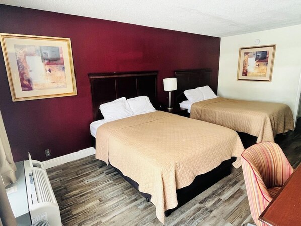 Een hotelkamer met twee bedden, een houten vloer, een rode accentmuur en ingelijste foto's.